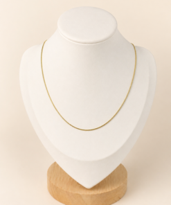 Cadena de acero quirúrgico dorado fina de 40 cm, exhibida sobre busto blanco con fondo neutro cálido.