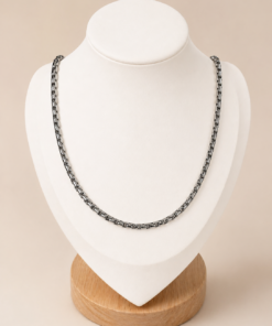 Cadena de acero quirúrgico eslabón chino de 50 cm sobre busto blanco con fondo neutro cálido.