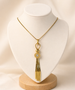 Cadena de acero quirúrgico dorado con dije de ojo turco y borla, exhibida sobre busto blanco con fondo neutro cálido.