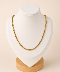 Cadena de acero quirúrgico dorado con eslabón chino de 45 cm, exhibida sobre busto blanco con fondo neutro cálido.