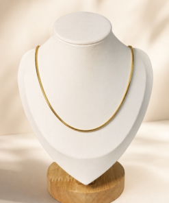 Cadena de acero quirúrgico dorado tipo serpiente exhibida sobre busto blanco con fondo neutro cálido.