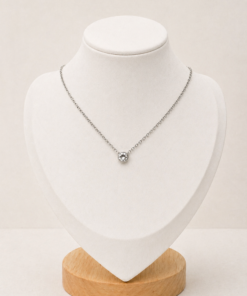 Cadena de acero quirúrgico con punto de luz, presentada sobre busto blanco con fondo neutro cálido.