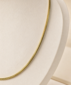 Cadena de acero quirúrgico dorado tipo serpiente exhibida mas de cerca sobre fondo neutro cálido.