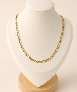 Cadena de acero quirúrgico dorado tipo Fígaro 3-1 de 60 cm, exhibida sobre busto blanco con fondo neutro cálido.