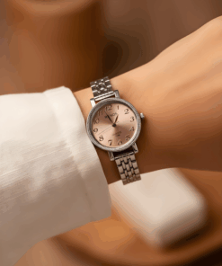 Mano exhibiendo reloj pulsera dama plateado fondo rosado