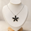 Cadena de plata 925 con dije de flor negra sobre busto blanco, diseño elegante y minimalista.