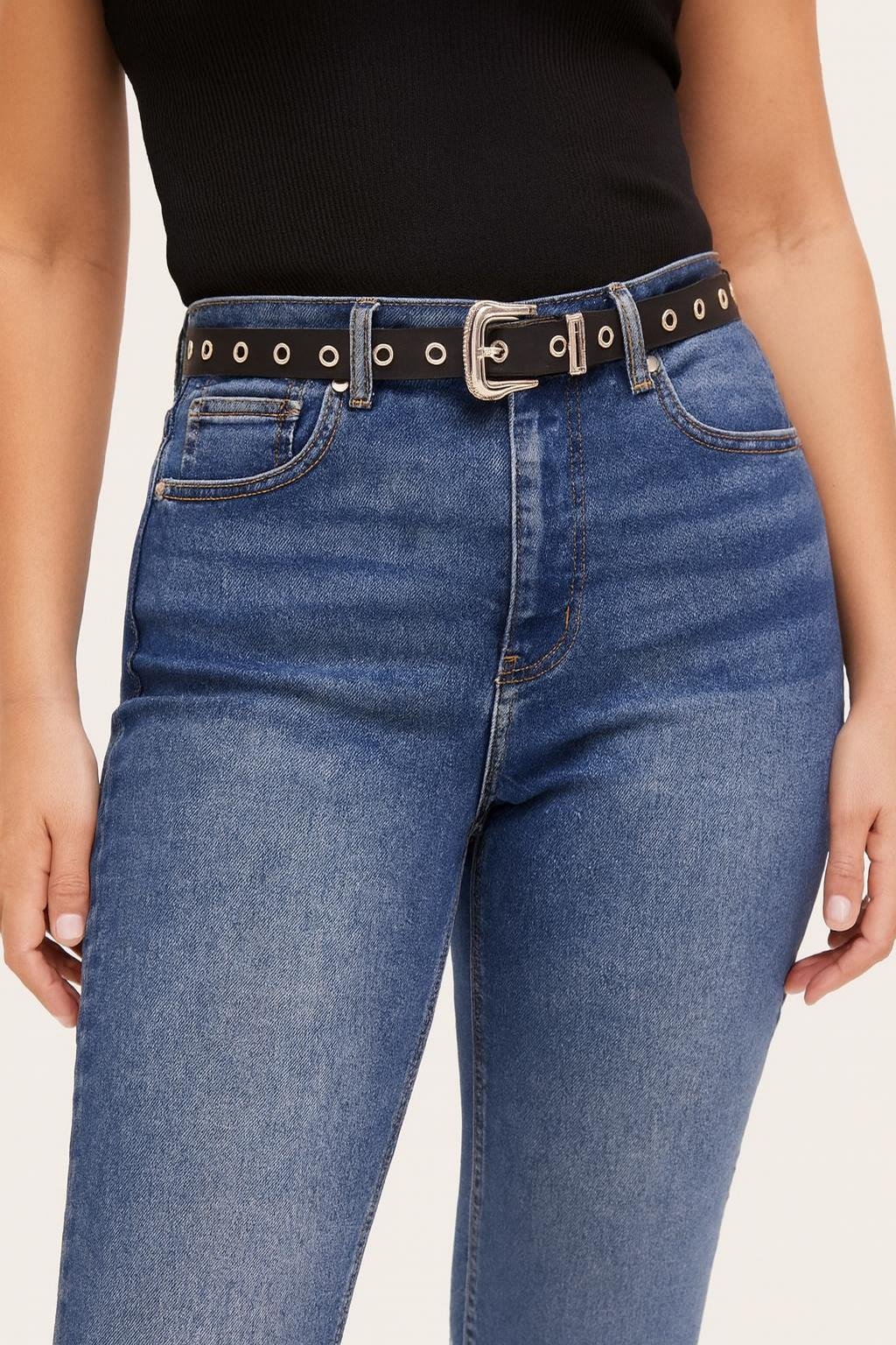 Cinto negro fino con ojalillos plateados para mujer, combinado con jean de tiro alto. Accesorio de moda versátil y moderno en Uruguay.