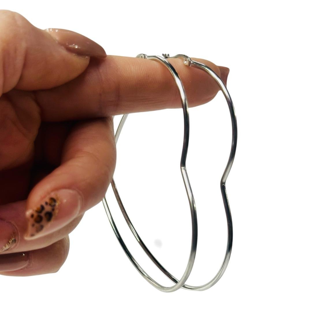 mano exhibiendo un par de aros con forma de corazon de acero quirurgico