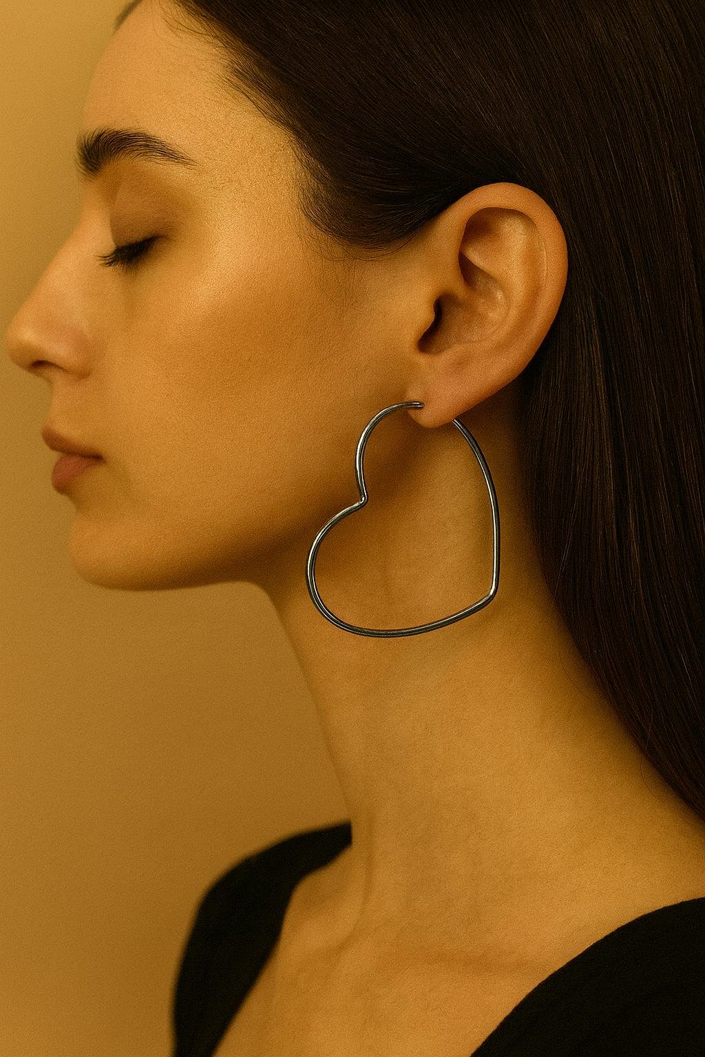 modelo de perfil exhibiendo caravanas aros con forma de corazon en acero quirurgico