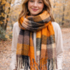 Modelo con Bufandón de tejido suave con flecos, ideal para looks abrigados de otoño e invierno, rayado naranja y negro