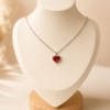 Cadena de acero quirúrgico con dije de corazón, exhibida sobre busto blanco con fondo neutro cálido elegante rojo.