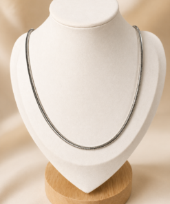 Cadena fina de acero quirúrgico plateado exhibida sobre busto blanco con fondo neutro cálido.