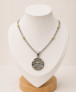 Cadena de plata con dije circular Ojo de Horus y double de oro, presentada sobre busto blanco.