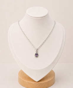 Cadena de plata 925 con dije pequeño de amatista ovalada, presentada sobre busto blanco con fondo neutro cálido.