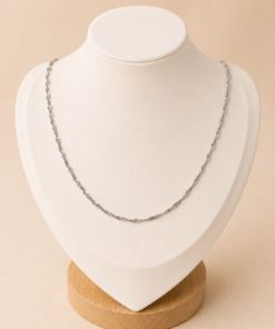 Cadena de acero quirúrgico plateado tipo Singapur de 45 cm sobre busto blanco con fondo neutro cálido.