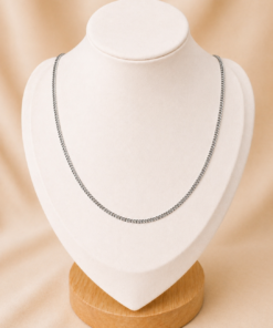 Cadena de acero quirúrgico plateado tipo grumet de 50 cm exhibida sobre busto blanco con fondo neutro cálido.