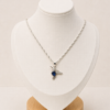 Cadena de plata 925 con dije de colibrí y circonia azul, exhibida sobre busto blanco con fondo neutro cálido.