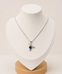 Cadena de plata 925 con dije de colibrí y circonia azul, exhibida sobre busto blanco con fondo neutro cálido.