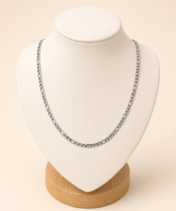 Cadena de acero quirúrgico plateado tipo Fígaro 3-1 fina de 50 cm exhibida sobre busto blanco con fondo neutro cálido.